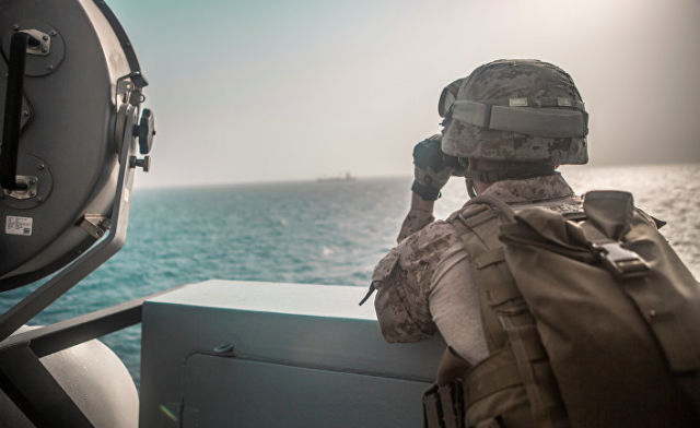 Американский военный смотрит в бинокль на корабль в Ормузском проливе