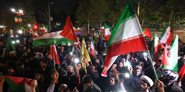 Демонстранты размахивают флагом Ирана и палестинскими флагами перед посольством Великобритании в Тегеране 14 апреля 2024 года после того, как Иран атаковал Израиль беспилотниками и ракетами