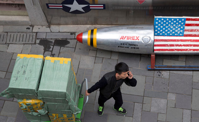 Мужчина с тележкой возле скамейки в виде ракеты с флагом США рядом с магазином в Пекине