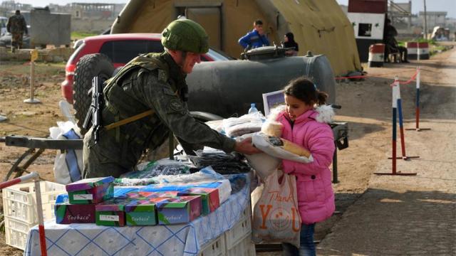 Военнослужащий российского центра по примирению враждующих сторон раздает гуманитарную помощь сирийским беженцам на территории гуманитарного коридора Абу-Духур в окрестностях провинции Идлиб