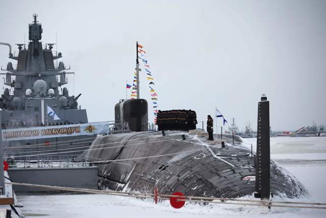 Военные моряки на атомном подводном крейсере «Император Александр III» во время торжественной церемонии подъема военно-морского флага на АО «ПО «Севмаш» в Северодвинске. На дальнем плане — фрегат «Адмирал Касатонов»