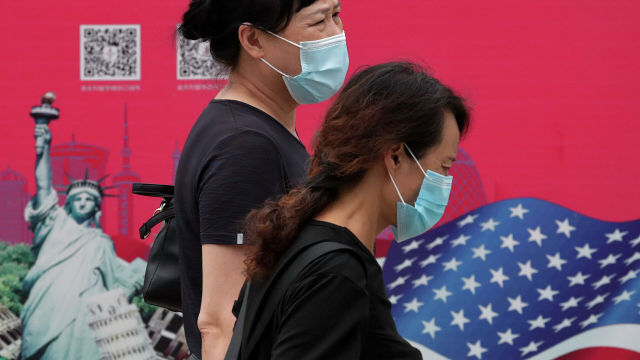 Женщины в защитных масках проходят мимо рекламного щита в Пекине